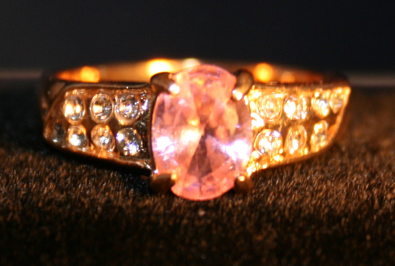 Oval pink gemstone. clear gemstones inlaid in two rows on the band