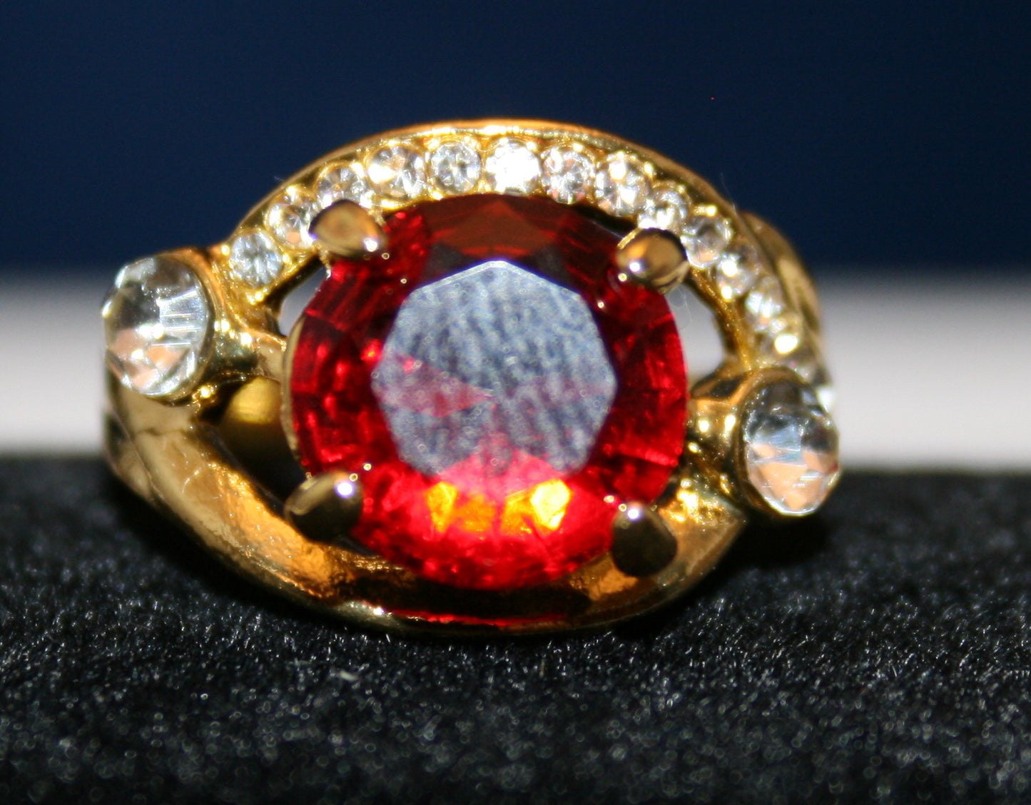 large round ruby red gemstone surrounded by two bands of clear stones