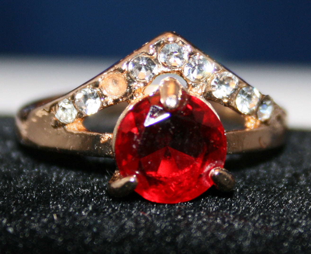 Small red circular gemstone with clear stones set in gold V-shape band