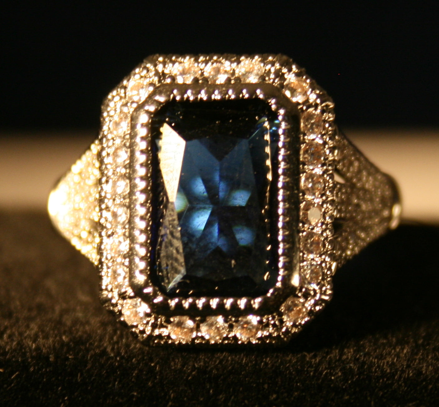 Rectangular blue gemstone signet ring with surrounding white stones.