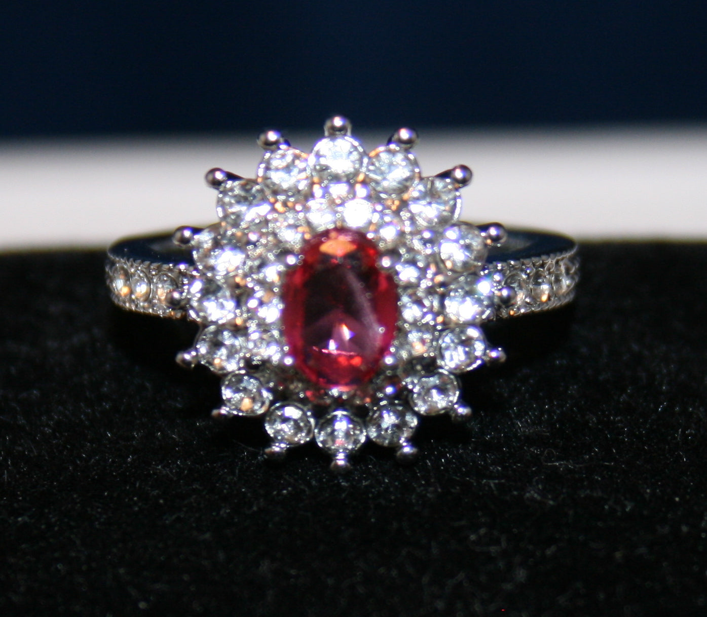 oval-shaped red gemstone, surrounded by a halo of smaller round white gemstones