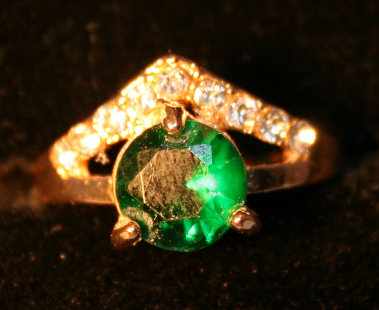 Emerald green gemstone in V-shaped band with inlaid stones